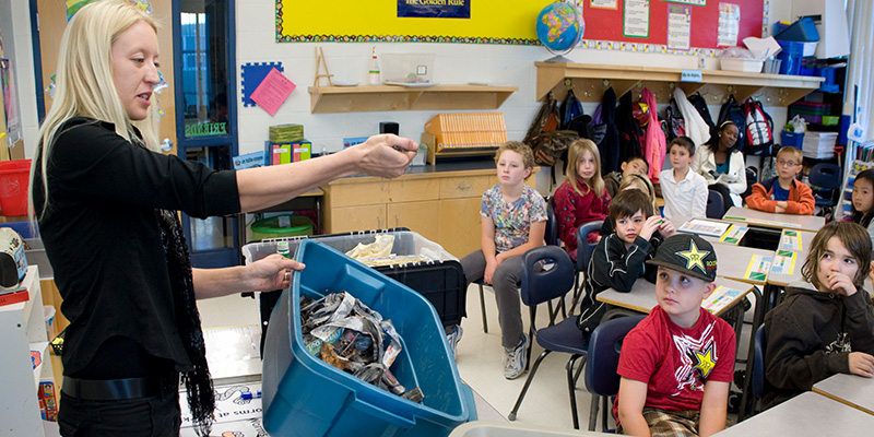 A classroom waste-education presentation with a recycling container